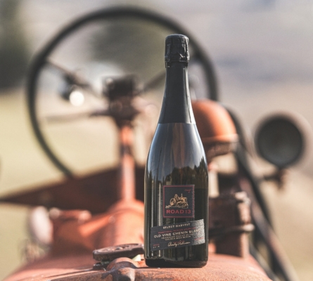 Road 13 Vineyards 2019 Old Vines Sparkling Chenin Blanc bottle standing on a vintage tractor with a softly blurred rural background.